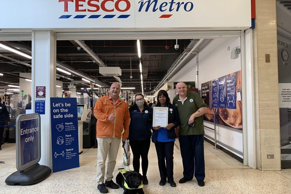 Photo shows George and Usef the wonder dog along with Tesco team members Rozita, Chez and Johnathan standing at the entrance to the Tesco store.